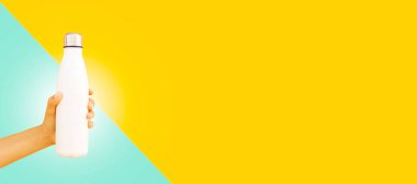 Çelik termo beyaz su şişesi tutan kadın. Arka planda sarı ve siyan renkli fotokopi alanı var. Panoramik pankart görünümü.