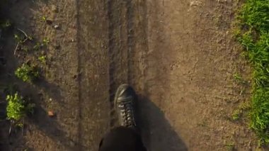 Kırsal yolda yürüyen genç bir adam. Siyah spor ayakkabılar ve kot pantolon giyen erkek bacaklarının yakın çekimi..