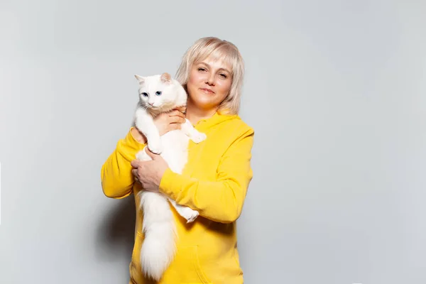 工作室肖像画的是一个快乐的金发女人 她抱着一只毛茸茸的猫 蓝眼睛 白色背景 身穿黄色毛衣 — 图库照片