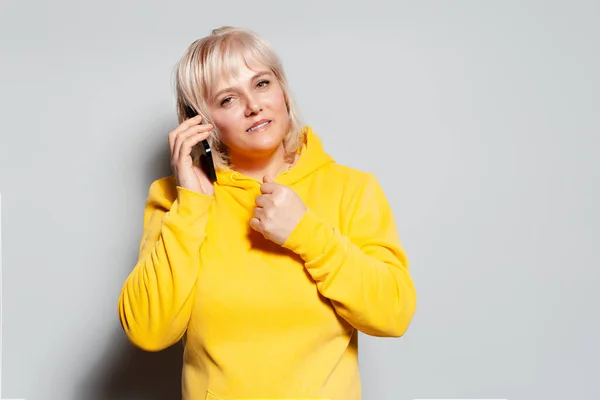 身着黄色毛衣 头戴智能手机 背景为白色的金发女子的工作室肖像 — 图库照片