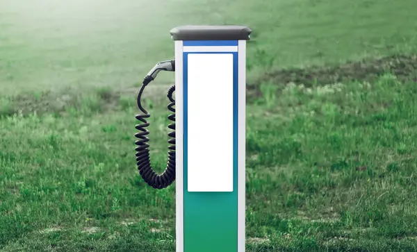 Electric car charger with blank on screen on background of green field. Mockup, environmental concept.