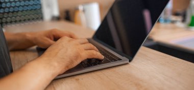 Modern dizüstü bilgisayarın klavyesinde daktilo eden erkek ellerinin yakın çekimi.