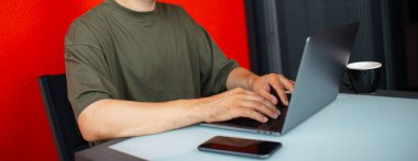 Dizüstü bilgisayarda çalışan genç bir adamın portresi, klavyeye yazı yazması, renkli kırmızı duvarın arka planında. İş adamları. Panoramik pankart görünümü.