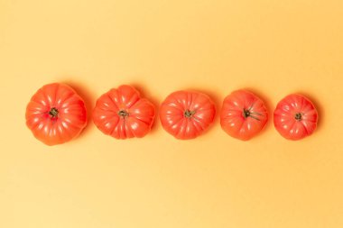 Pastel sarısı arka planda pembe domateslerin yakın plan görüntüsü.