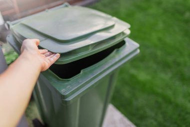 Erkek el arka bahçedeki çöpler için büyük yeşil plastik bir kutu açar. Yakın çekim görünümü.