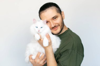 Beyaz arka planda beyaz Maine Rakun kedisi olan gülümseyen genç adamın portresi.