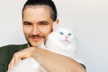 Beyaz arka planda mavi gözlü, beyaz tüylü kediye sarılan genç adamın portresi..