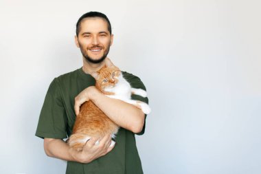 Beyaz arka planda pofuduk kırmızı beyaz kediyi kucaklayan mutlu genç adamın portresi..