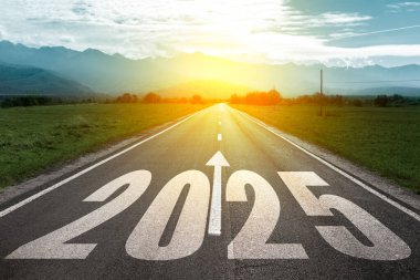 Yeni yıl 2025 konsepti. 2025 'in metni ve asfalt yolun ortasında gün batımı ve dağların arka planında yazılmış ok..