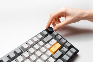 Kadın el, klavyedeki ses kontrolünü sarı ve gri anahtar başlığıyla, beyaz arkaplanda ayarlıyor.