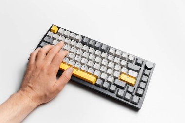 Gri ve sarı tuş kapağıyla klavyede yazan erkeğin üst görünümü.