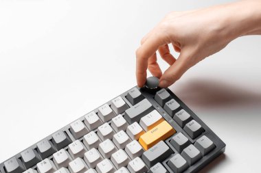 Kadın el, klavyedeki ses kontrolünü sarı ve gri anahtar başlığıyla, beyaz arkaplanda ayarlıyor.