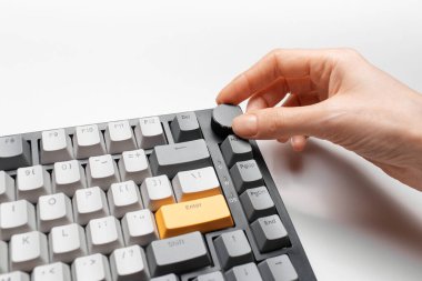 Kadın el, klavyedeki ses kontrolünü sarı ve gri anahtar başlığıyla, beyaz arkaplanda ayarlıyor.