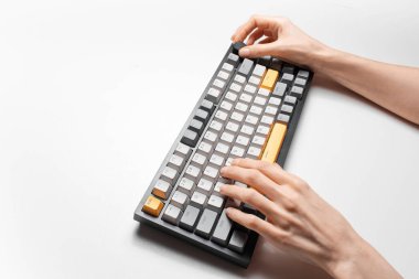 Beyaz arkaplanda, gri ve sarı anahtar kapaklı mekanik klavyede yazan kadın elleri.