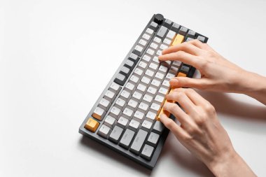 Beyaz arkaplanda, gri ve sarı anahtar kapaklı mekanik klavyede yazan kadın elleri.