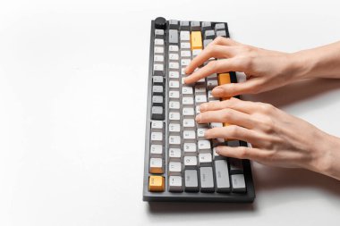 Beyaz arkaplanda, gri ve sarı anahtar kapaklı mekanik klavyede yazan kadın elleri.