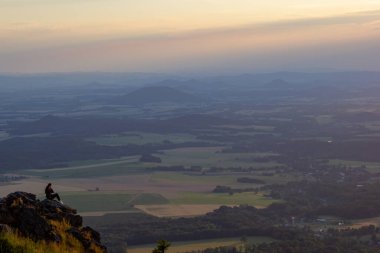 Yalnız bir kız bir kayanın üzerinde oturuyor ve şafakta dağlara bakıyor..