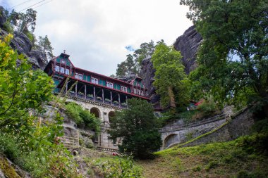 Mavi gökyüzü altında yeşil ağaçları olan kayalık dağlar arasında tarihi mimari yapı