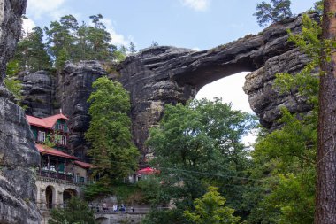 Mavi gökyüzü altında yeşil ağaçları olan kayalık dağlar arasında tarihi mimari yapı
