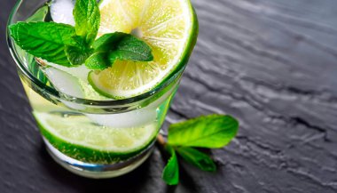 Yeşil limonlu mojito kokteylinin üst görüntüsü, koyu arkaplanda limon ve nane şekeri.