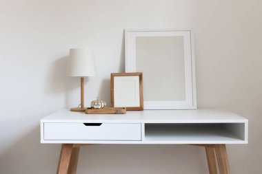 Minimalist masa lambası ve gümüş süslemeli balkabağı ile ahşap tepsi ile beyaz masanın üzerinde boş yatay ahşap çerçeveler. Çağdaş iç tasarım, doğal renkler.