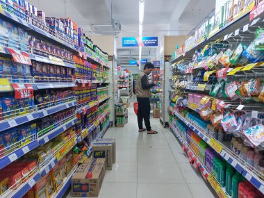 Alışveriş sepeti taşıyan bir adam süpermarket rafından ürün seçiyor.