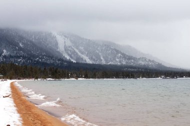 Arkasında orman ve karlı dağ olan göl.