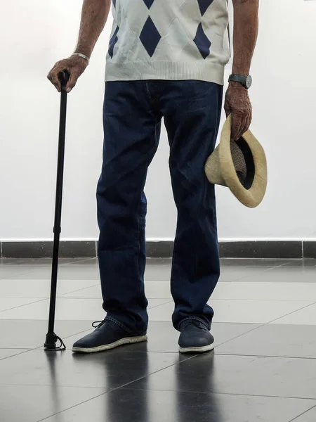 Old man holding walking stick in one hand and hat in other
