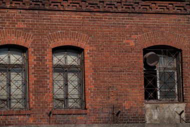 Üç kemerli pencereli kırmızı tuğla duvar. Çiçek desenli, karmaşık metal ızgaralar..