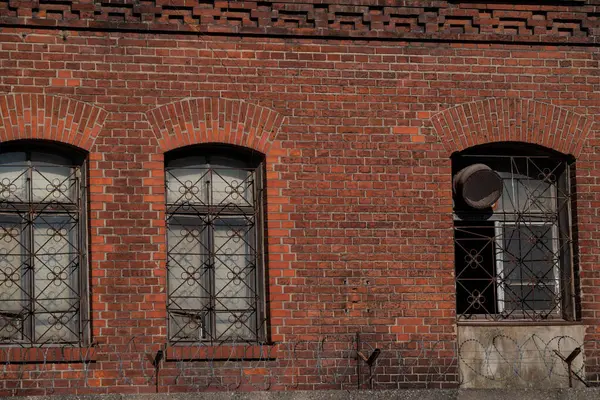 Üç kemerli pencereli kırmızı tuğla duvar. Çiçek desenli, karmaşık metal ızgaralar..