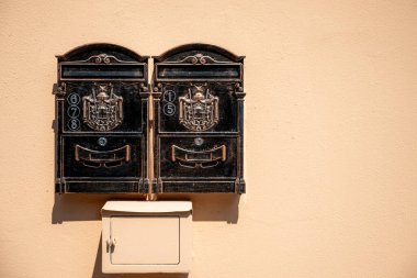 Duvara monte edilmiş iki antika metal posta kutusu. Her kutuda süslü bir arma var..