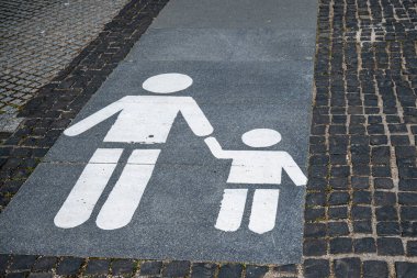 Kaldırıma bir yaya sembolü çizilmiş, stilize bir yetişkinin bir çocuğun elini tuttuğunu gösteren bir yürüyüş yolu..
