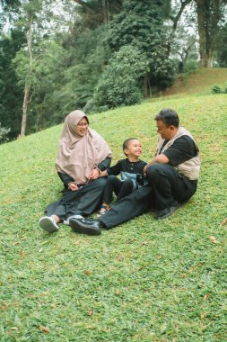 Baba, anne ve çocuğu olan aile çimlerin üzerinde oturup birlikte oynuyorlar. 