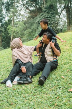 Baba, anne ve çocuğu olan aile çimlerin üzerinde oturup birlikte oynuyorlar.