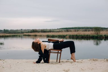 Moda fotoşopu, sanatsal ifade ve doğal güzellik sergilenirken kumlu bir nehir kıyısındaki bir sandalyede poz veren manken.
