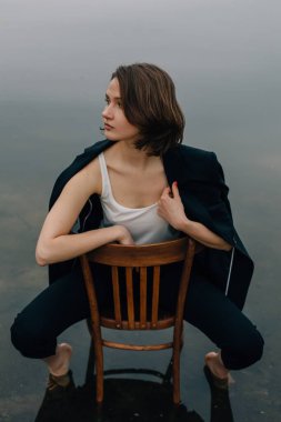 Suyun içindeki sandalyede çıplak ayakla poz veren manken doğada sisli, karamsar atmosferli bir fotoğraf çekimi sırasında.