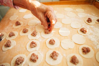 Yaşlı kadın ustalıkla kıyma parçalarını küçük hamur çemberlerine yerleştiriyor, hamur işi yapma sürecinde bir sonraki adıma özenle hazırlanıyor.