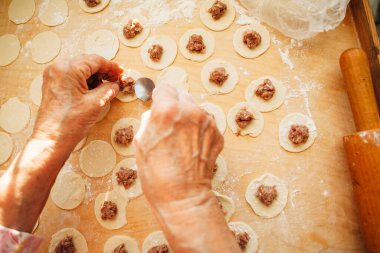 Kırış kırış eller tahtanın üzerinde kıymalı hamur köftelerini hazırlarken çay kaşığı kullanarak geleneksel mutfak becerilerini sergiliyorlar.