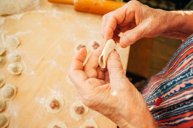 Buruşuk eller ahşap bir tahtanın üzerinde etle doldurulmuş hamur köftelerini ustalıkla şekillendiriyor. Geleneksel mutfak uygulamalarına bir bakış.
