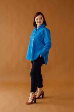 40 'larında bir iş kadınının stüdyo portresi. Şık bir mavi gömlek ve siyah pantolon giyiyor. Kendine güveni ve profesyonelliği var.