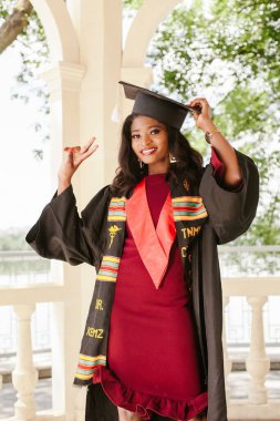 Genç bayan doktor mezuniyeti dışarıda kutluyor, siyah bir elbise ve havan topu giyiyor, başarısından gurur ve neşe saçıyor.