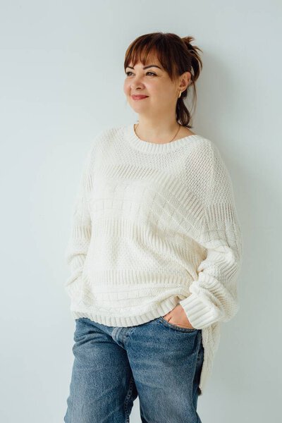 Studio portrait of a businesswoman in her 40s, exuding confidence in a casual sweater and jeans, showcasing a relaxed yet professional image