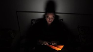 A girl in bed in a dark room working on a notebook 