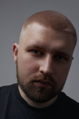 Millennial 'da kısa saçlı, sakallı, kulaklarında küpeleri olan bir adamın portreleri.