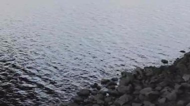 Nehir ya da göl kıyısında dokulu ve yansıtıcı su yüzeyi olan kayalık bir sahil.