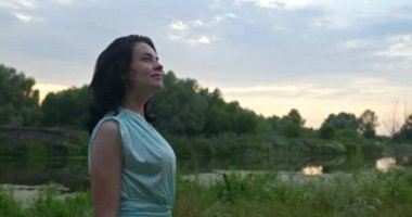 Mutlu kadın dinlenmeyi seviyor. Nehir kenarındaki doğada dinlenin. Yaz sezonu günbatımı. Kırsal Ülke Sahnesi 4K