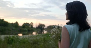 Çiçekli Kadın Sunset 'e bak, Doğanın Yakınındaki Nehir' de Dinleniyor. Yaz sezonu. Kırsal Ülke Sahnesi 4K