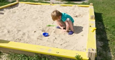 Sandbox 'ta oynayan şirin küçük çocuk. Çocuk oyun parkında kumla oynuyor. Parlak Güneşli Yaz Tatil Sezonu Çocukluğu. 4K 10-bit Yavaş çekim 60 fps