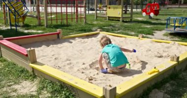 Sandbox 'ta oynayan şirin küçük çocuk. Çocuk oyun parkında kumla oynuyor. Parlak Güneşli Yaz Tatil Sezonu Çocukluğu. 4K 10-bit Yavaş çekim 60 fps