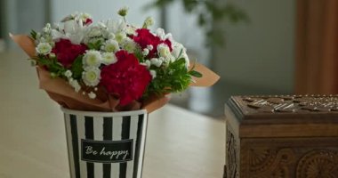 Salondaki Masa 'daki Tabutun yanındaki Çiçek Buketi Süslü Kutusu' na yakın çekim. Pencere Işığı. 4K 10 bit